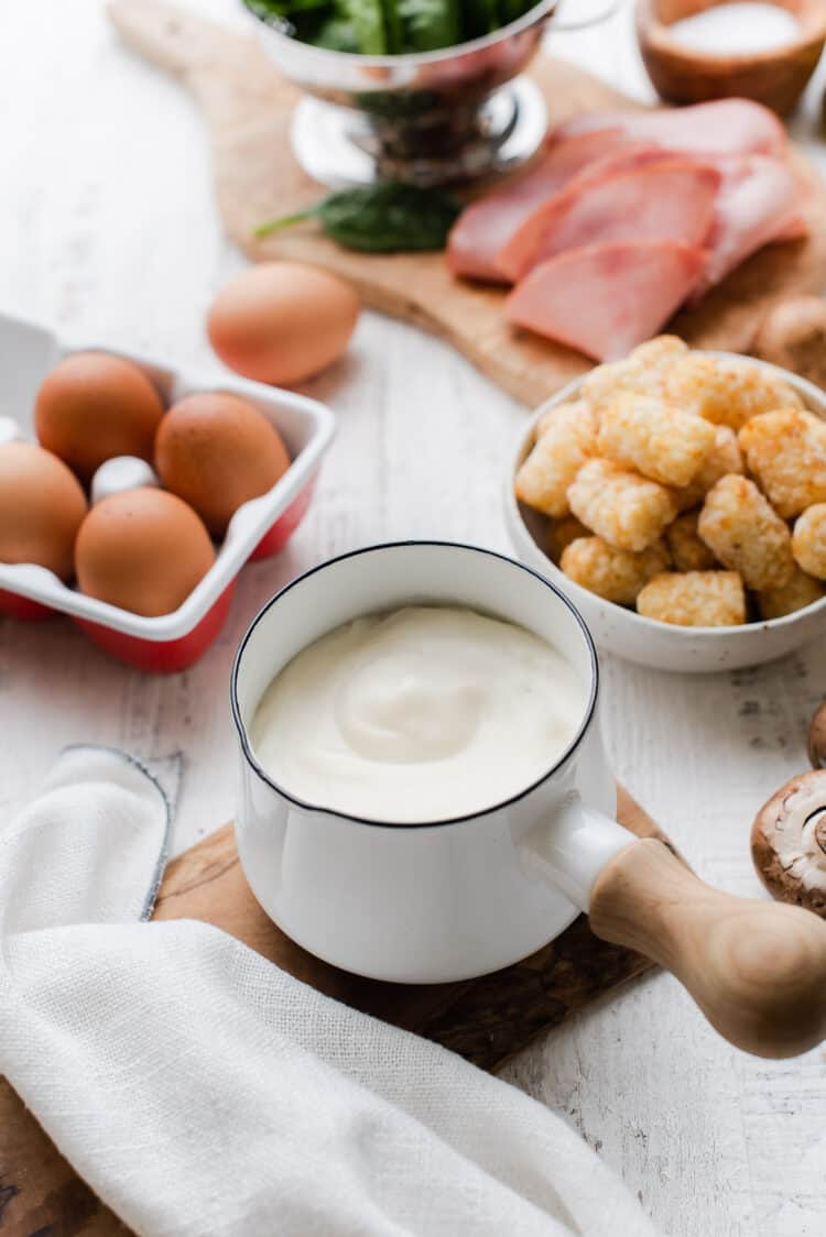 Biscuit gravy in a small white sauce pan with ingredients for Tater Tot Breakfast Casserole