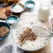 Mixing chopped pecans into a bowl of flour with a whisk.