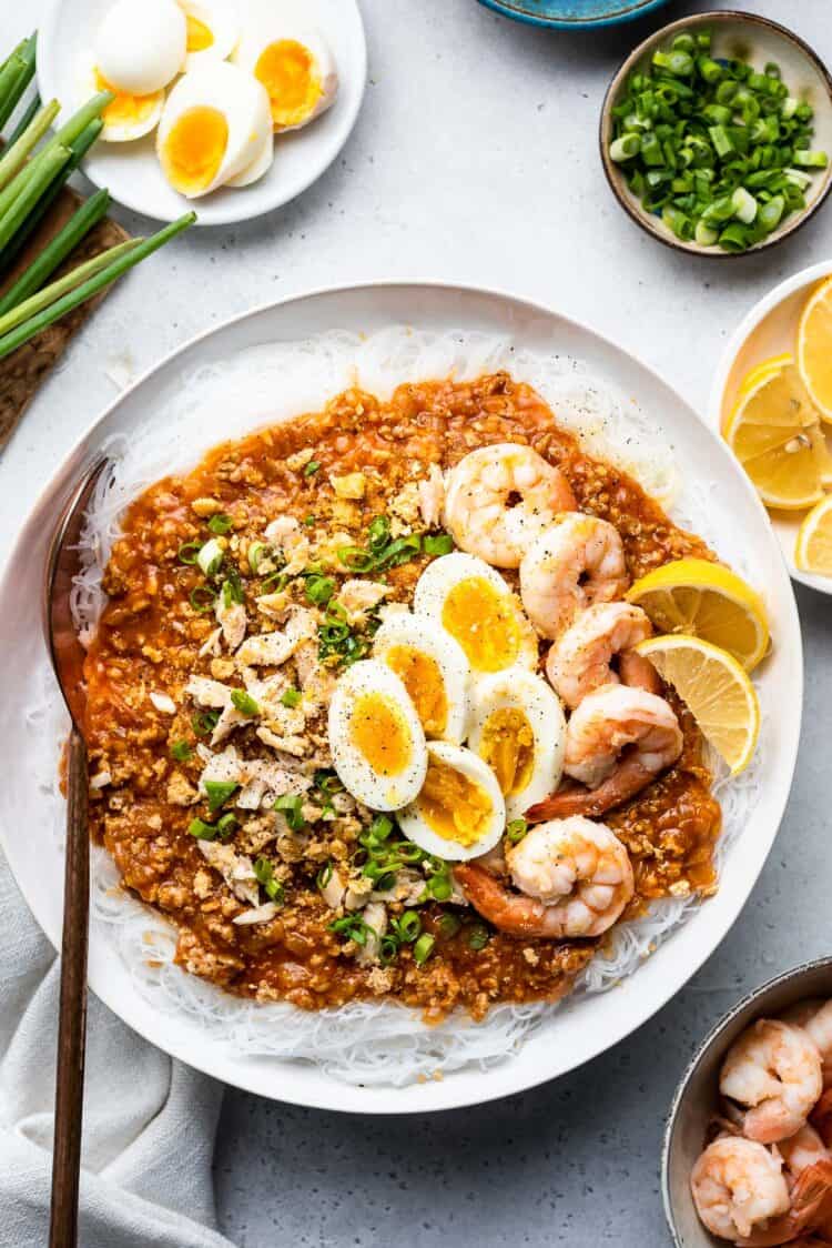 Pancit Palabok in a white bowl garnished with shrimp and hard boiled eggs.