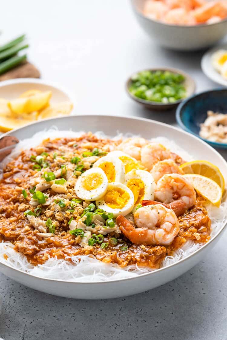 Pancit Palabok in a white bowl garnished with shrimp and hard boiled eggs.