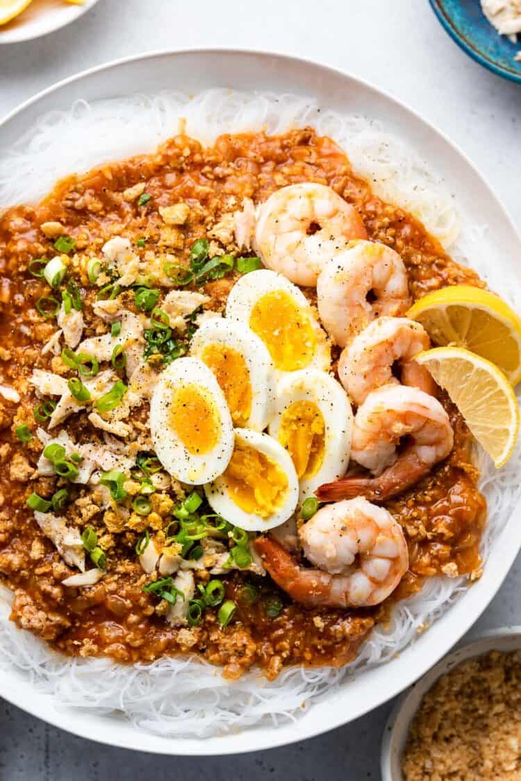 Pancit Palabok in a white bowl garnished with shrimp and hard boiled eggs.