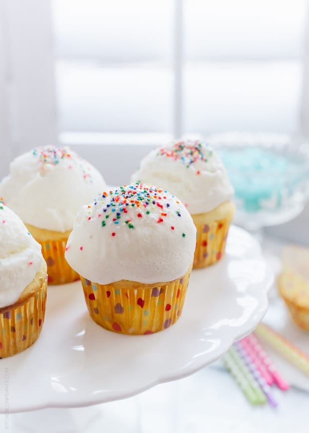 Yellow cupcakes topped with large scoops of ice cream and sprinkles.