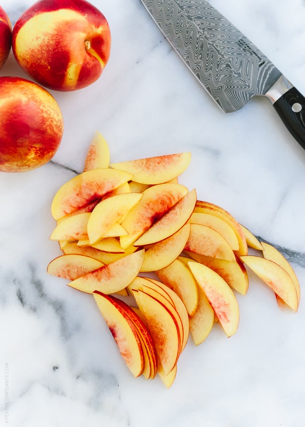 Whole and sliced nectarines on a white surface.