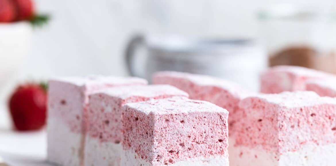 Homemade Strawberry Vanilla Marshmallows sliced on a white marble cutting board.