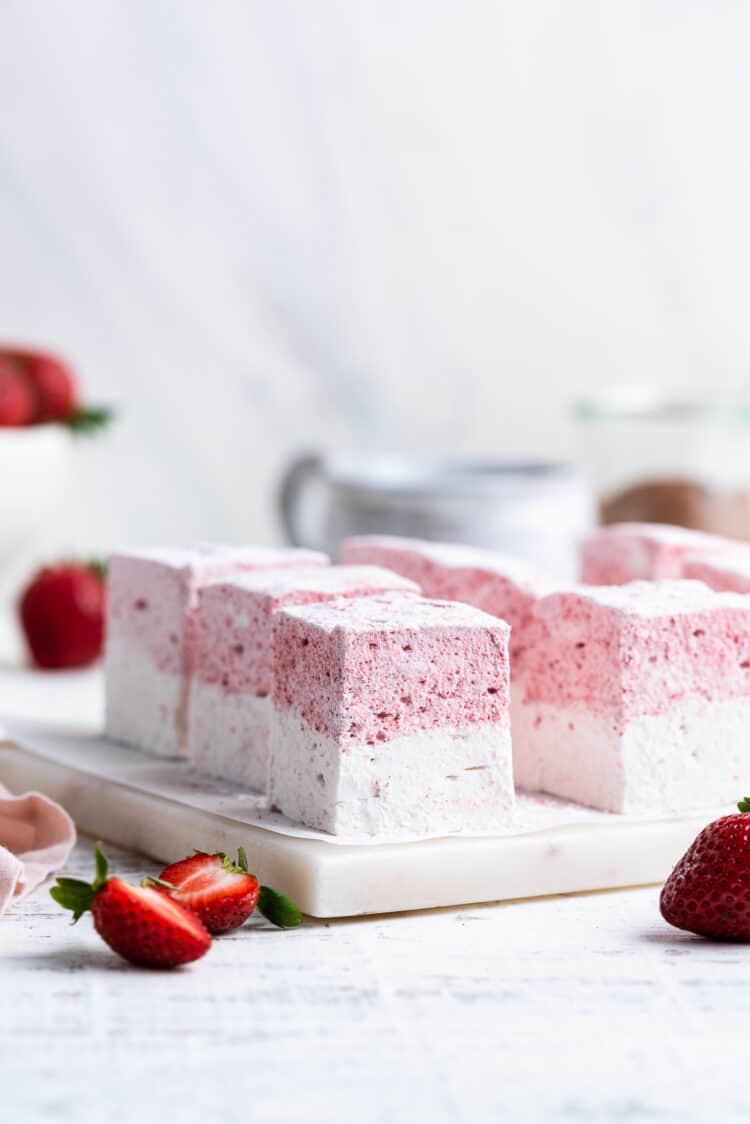 Homemade Strawberry Vanilla Marshmallows sliced on a white marble cutting board.
