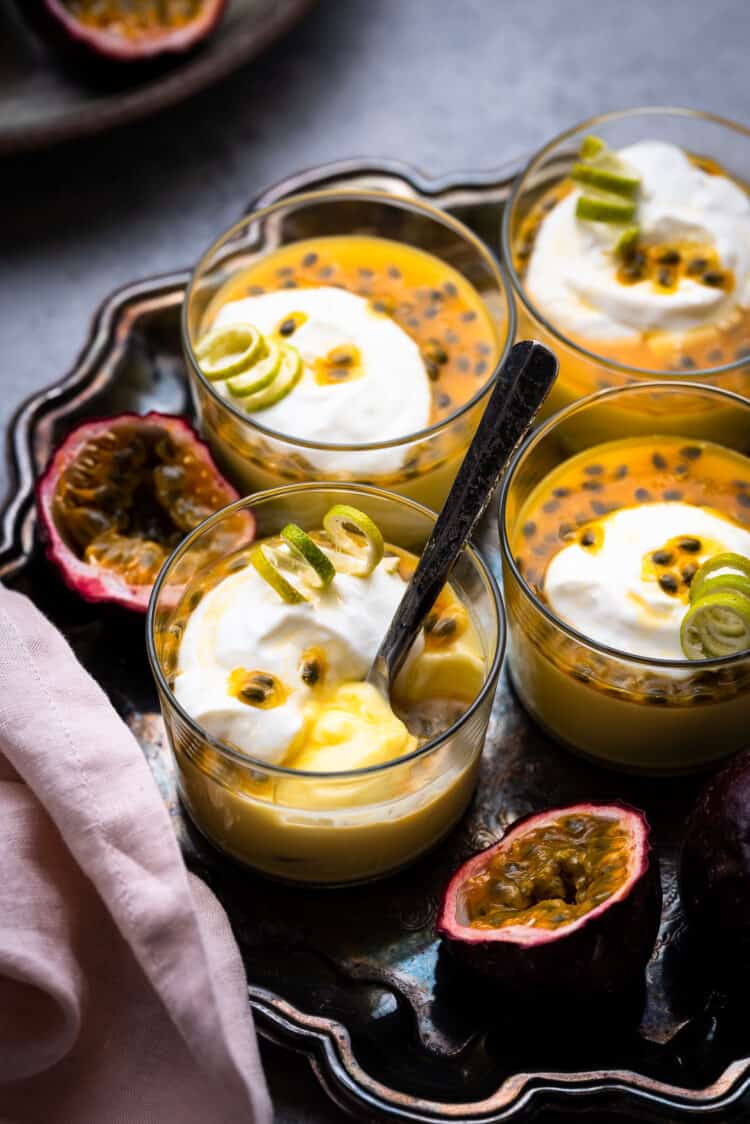 Passion fruit posset with a spoon on a tray with fresh passion fruit.