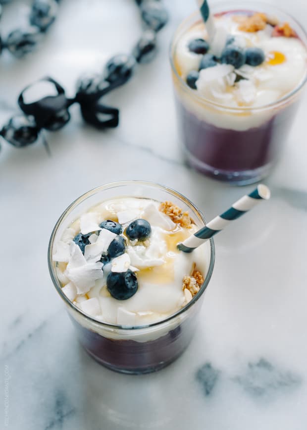 Two purple Açaí Smoothies topped with yogurt, coconut, and berries.