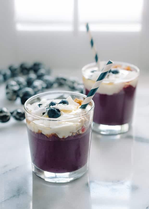 Two purple Açaí Smoothies topped with yogurt, coconut, and berries.