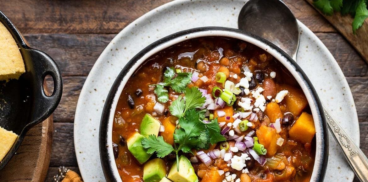 Kabocha Squash Chili in a bowl, garnished with avocado, cheese, red onion, green onion, and cilantro.