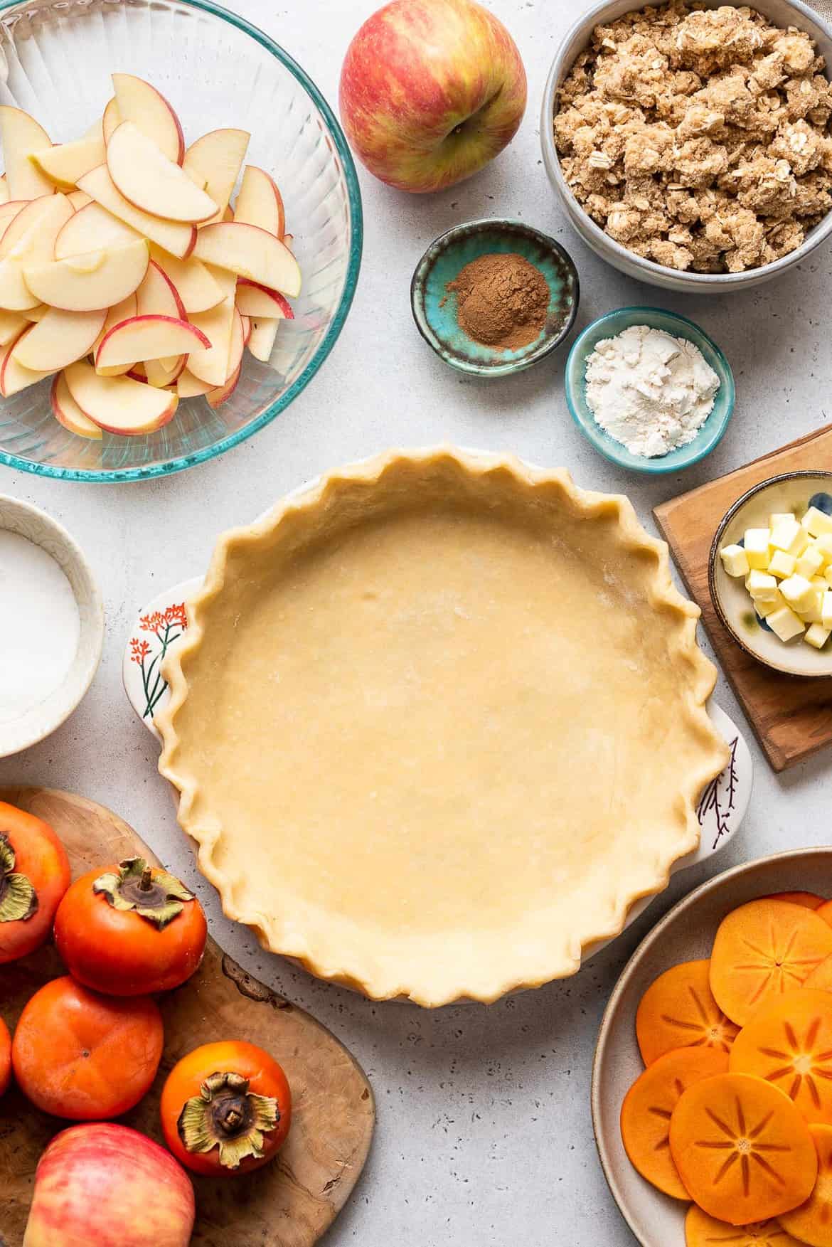 Ingredients for Persimmon Apple Crumb Pie with pie dough crimped in pie plate.