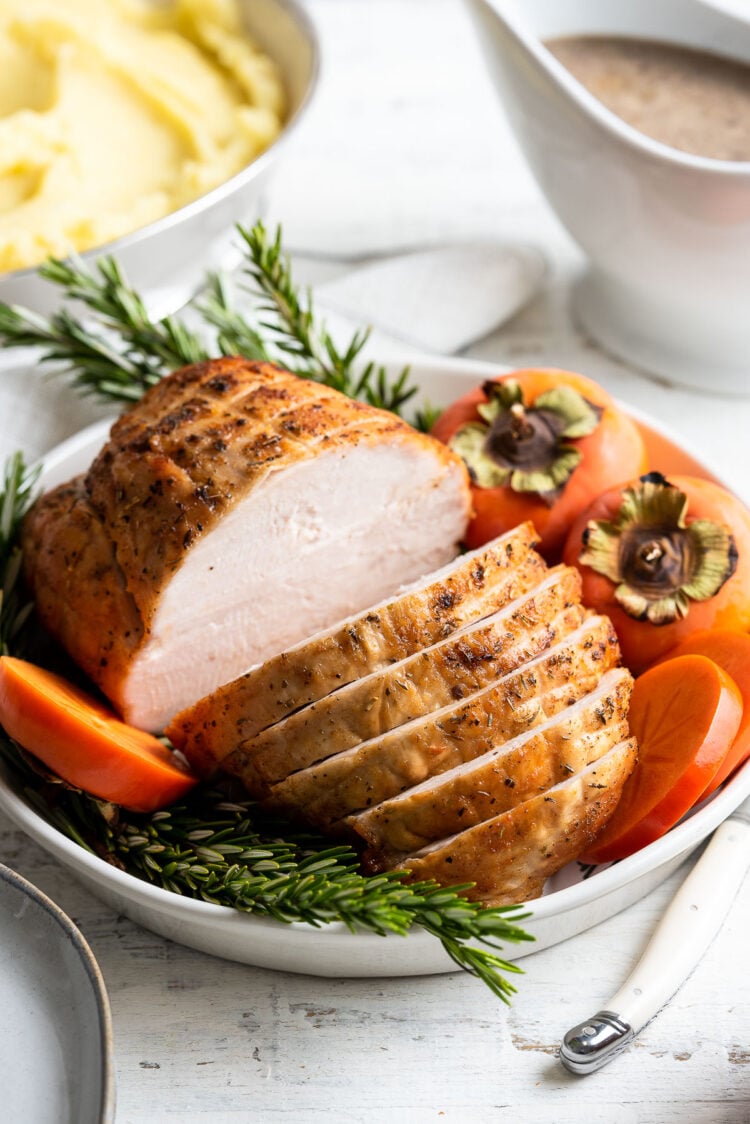 Roasted Boneless Turkey Breast sliced on a platter garnished with rosemary and persimmons.