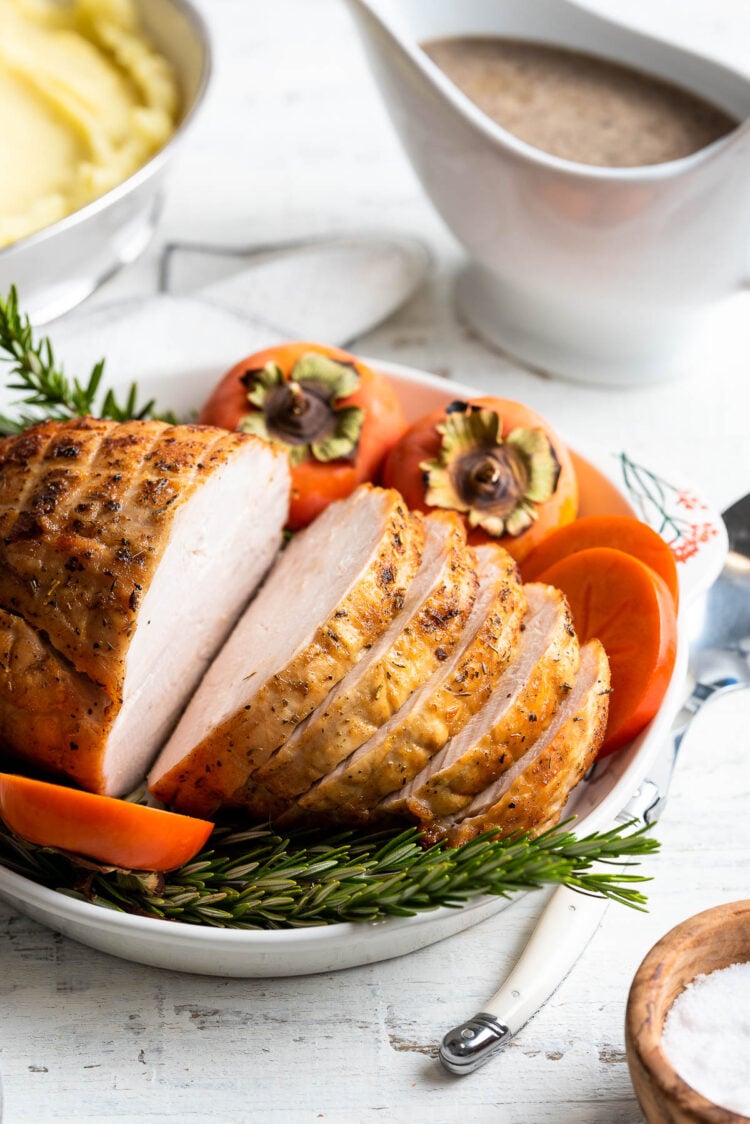 Roasted Boneless Turkey Breast sliced on a platter garnished with rosemary and persimmons.