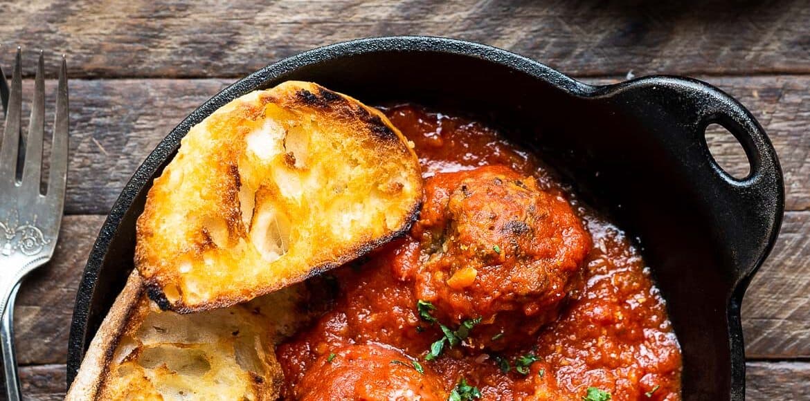 A black dish filled with marinara sauce, meatless mushroom meatballs, and two slices of Texas toast.