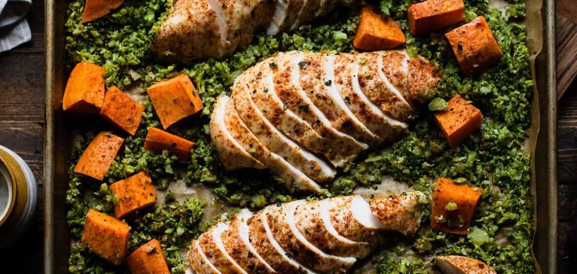 Baked broccoli rice, sweet potatoes, and chicken breast on a large baking tray.