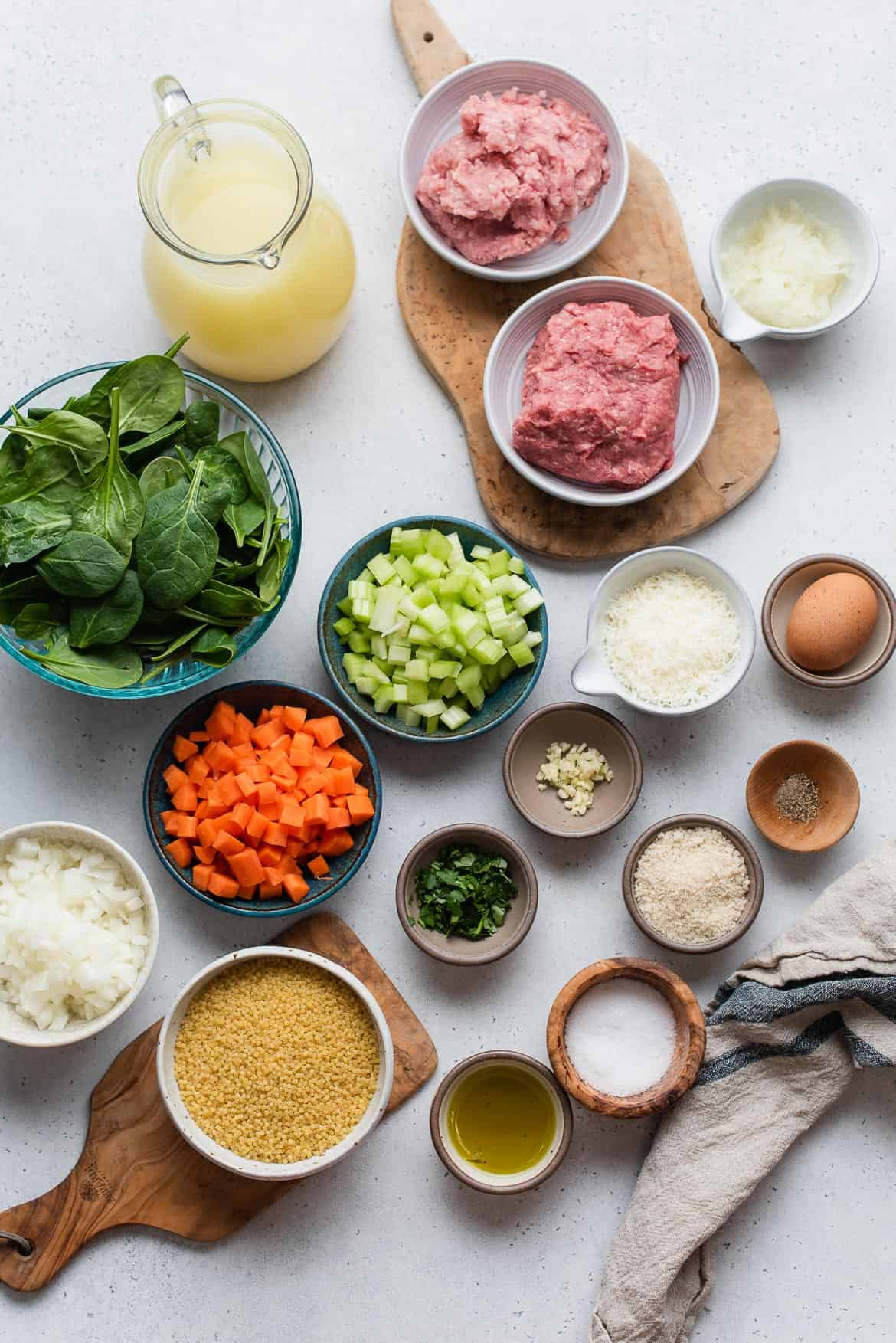 Ingredients for Italian Wedding Soup arranged in variety of small bowls including: chopped onion, carrots, celery, meat, and seasonings.