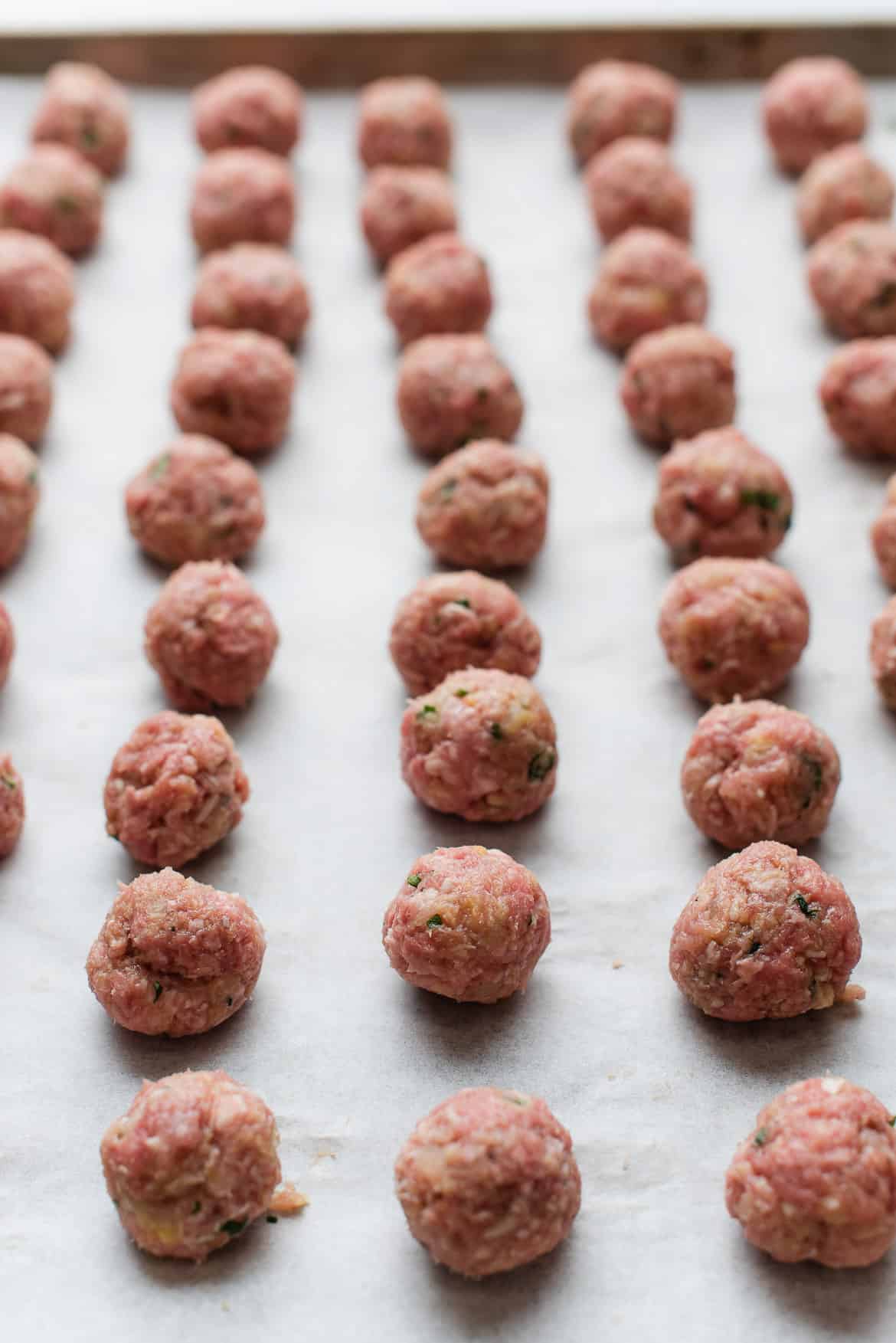 Small homemade meatballs ready to cook on a lined baking tray.