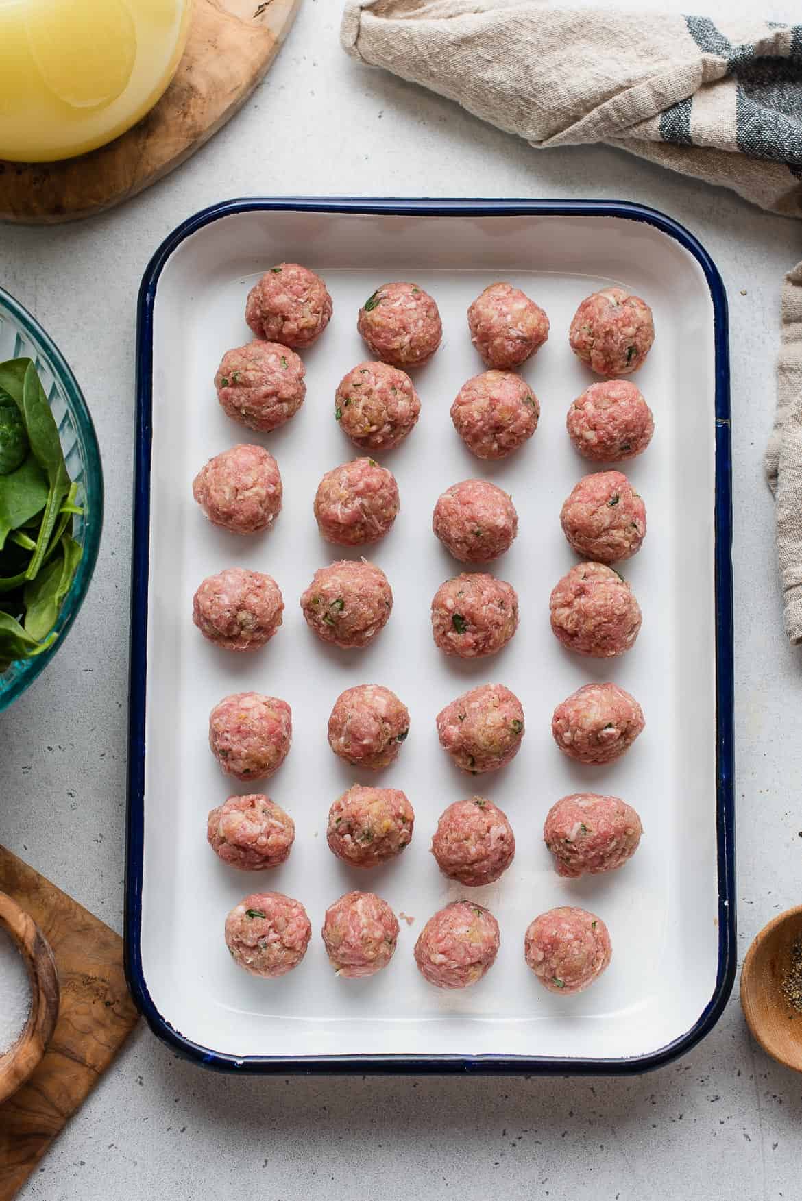 Homemade meatballs lined up on a rectangular pan, ready to cook.