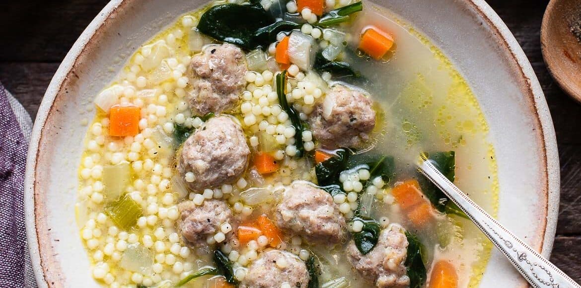 Italian Wedding Soup with acini di pepe pasta, homemade meatballs, spinach, and chopped vegetables in a bowl with a spoon.