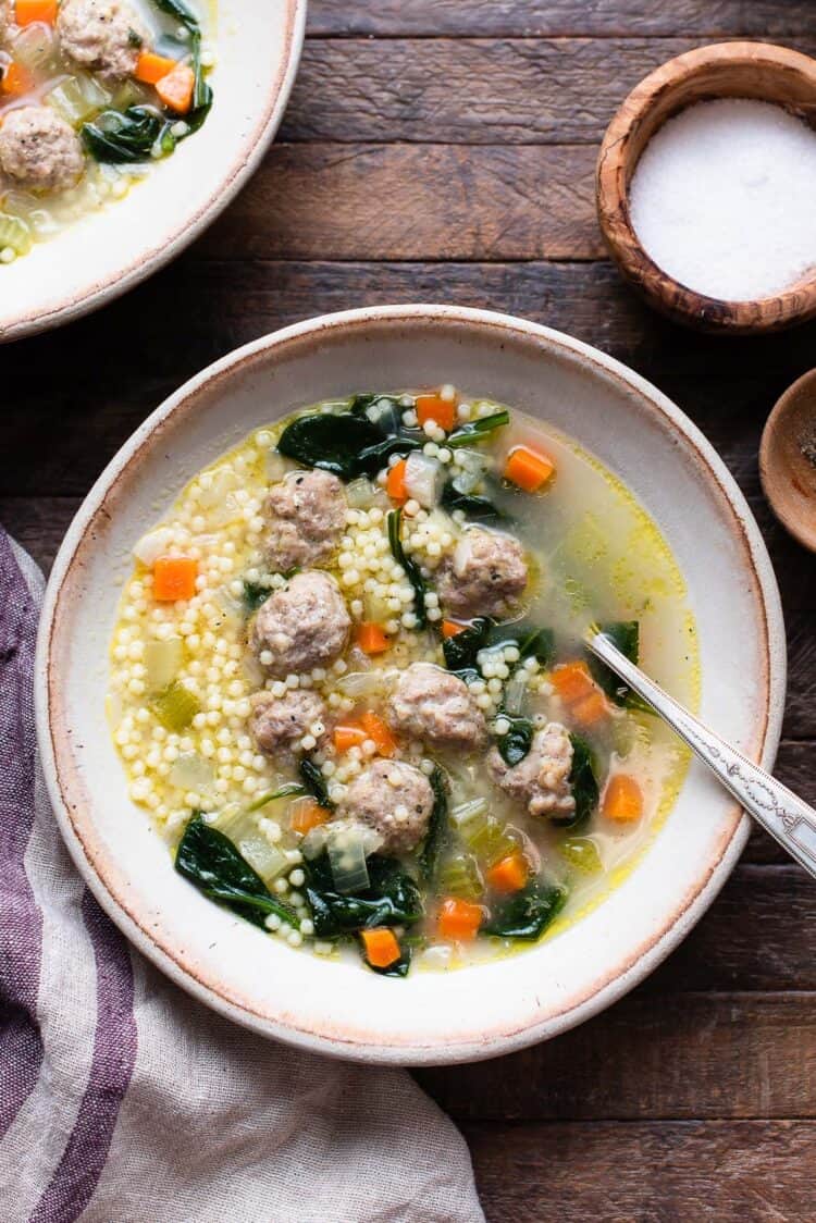 Italian Wedding Soup with acini di pepe pasta, homemade meatballs, spinach, and chopped vegetables in a bowl with a spoon.