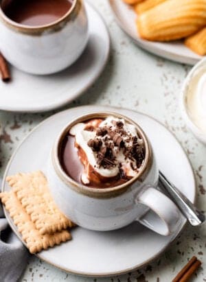 European Hot Chocolate in a mug with whipped cream, chocolate shavings, and served with cookies.