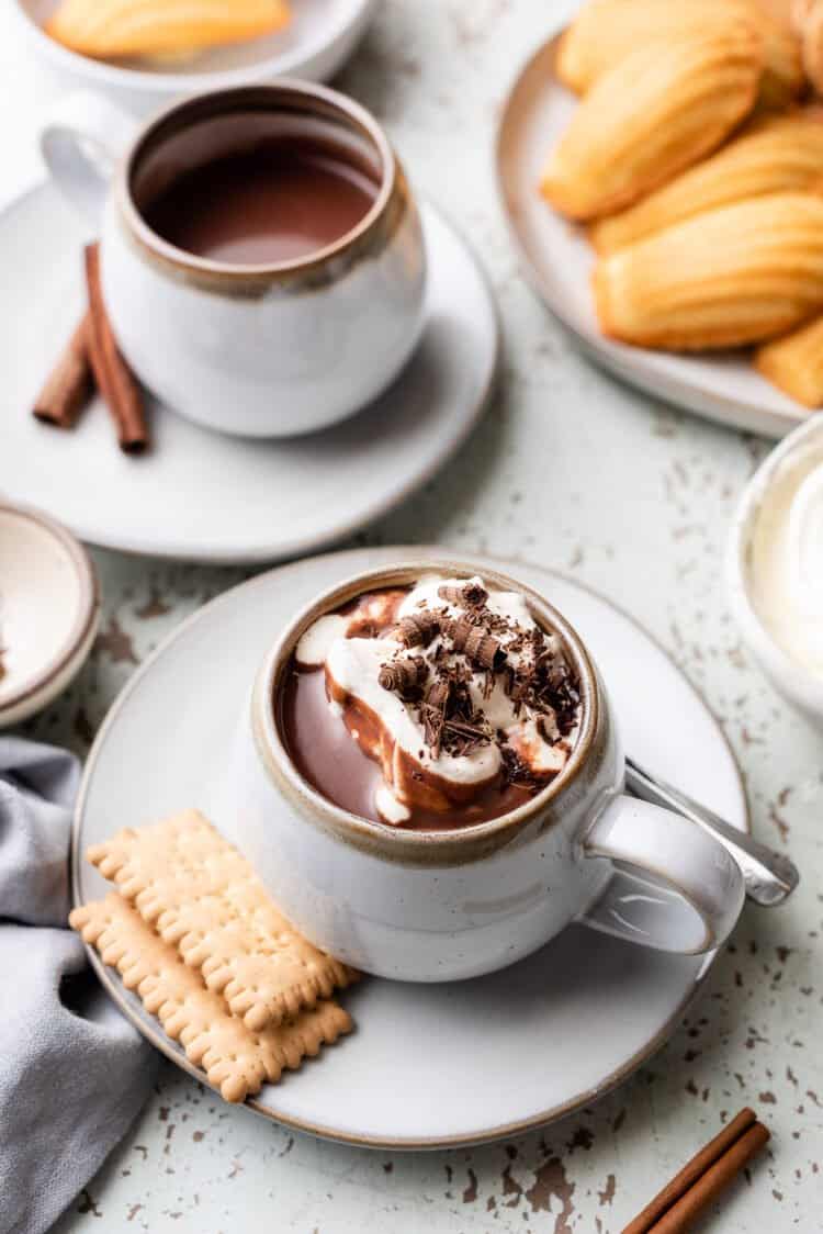 European Hot Chocolate in a mug with whipped cream, chocolate shavings, and served with cookies.