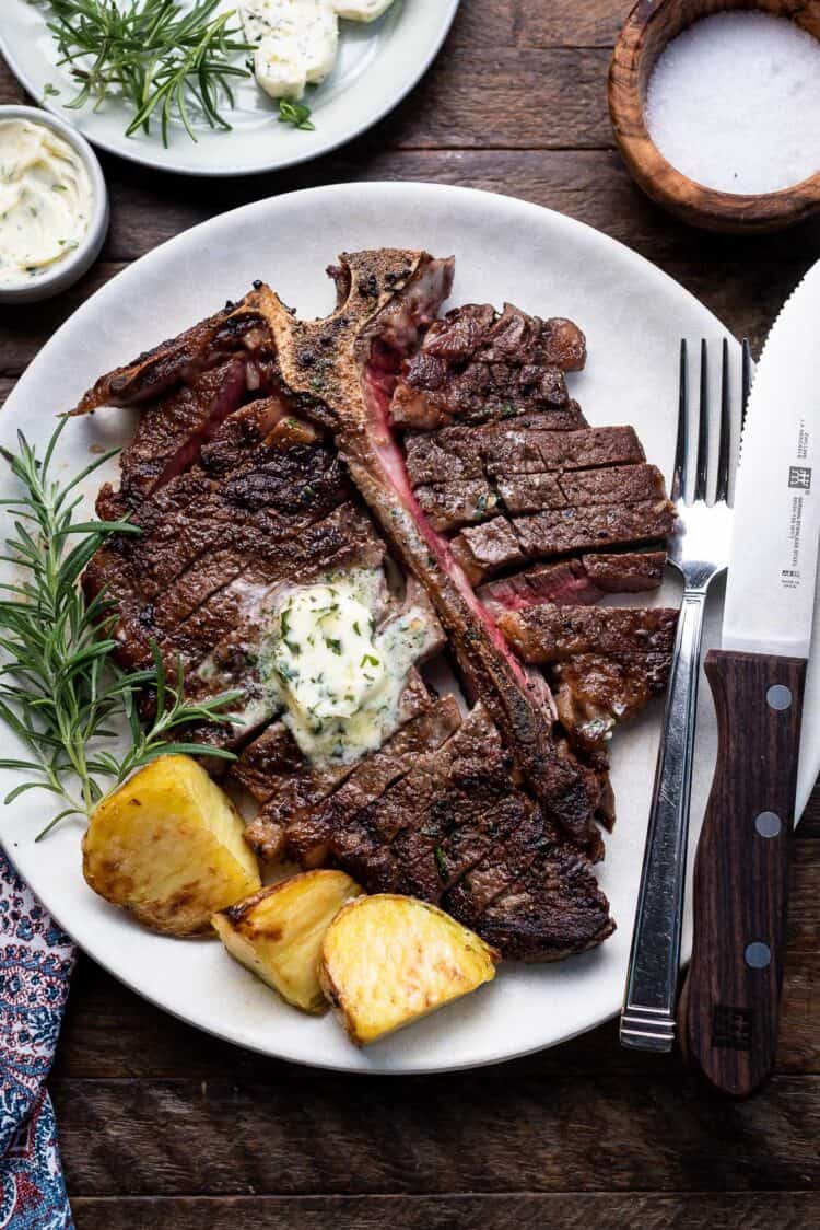 Angus Beef Steak Recipe with Garlic Herb Compound Butter, with potatoes and rosemary garnish on a plate.