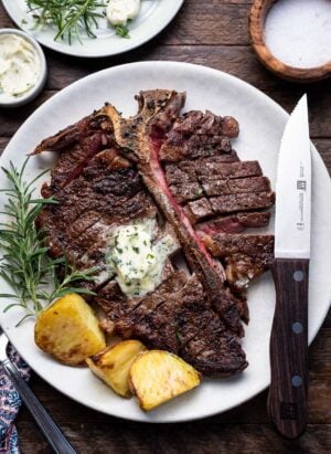 Angus Beef Steak Recipe with Garlic Herb Compound Butter, with potatoes and rosemary garnish on a plate.