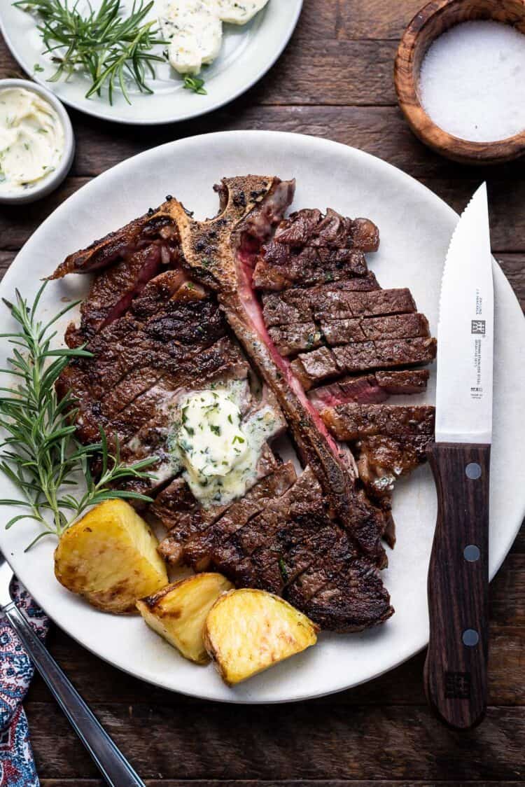 Angus Beef Steak Recipe with Garlic Herb Compound Butter, with potatoes and rosemary garnish on a plate.