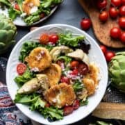 Artichoke Salad with Fried Mozzarella, tomatoes, and salad greens in a white bowl.