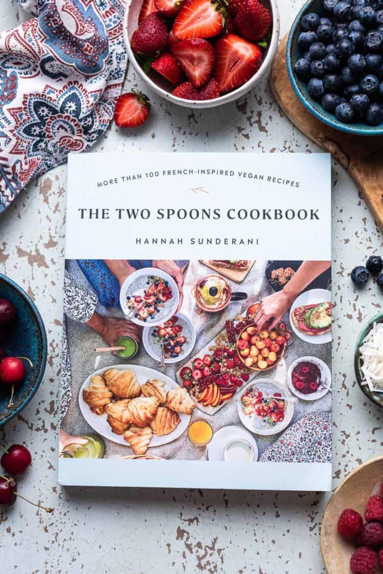 The Two Spoons Cookbook by Hannah Sunderani on a table with fresh fruit