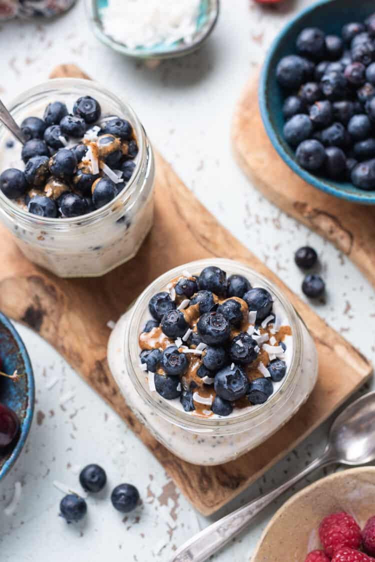 Blueberry Muffin Overnight Oats with fresh blueberries, almond butter and coconut flakes in a jars.