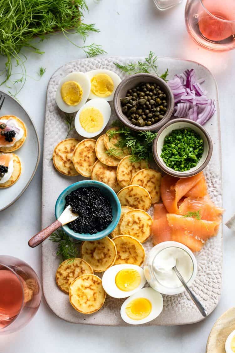 Caviar and Blini Board with smoked salmon, toppings, and hardboiled eggs.
