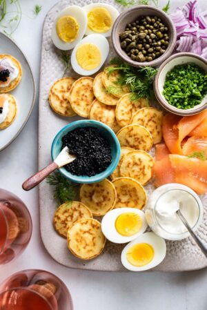 Caviar and blini board with smoked salmon, creme fraiche, chives, capers, and hardboiled eggs on a platter.