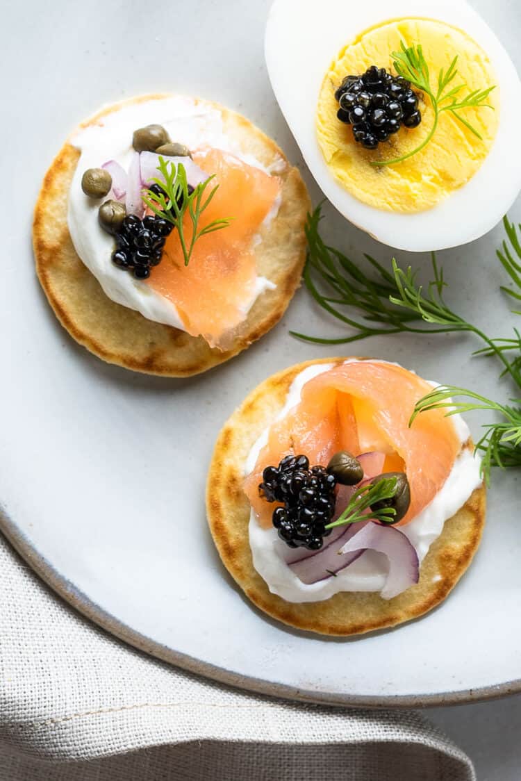 Caviar and blini bites with smoked salmon, red onion, capers and dill on a plate.