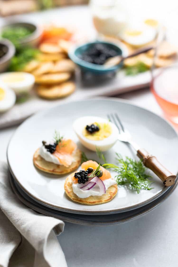 Caviar and blini with smoked salmon on an appetizer plate with a small fork.