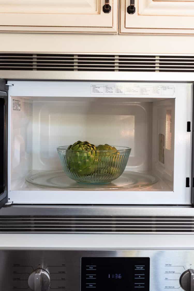 Two artichokes in a glass bowl in the microwave.