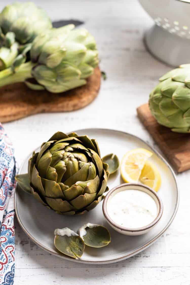 Steamed artichoke on a plate next to dipping sauce.