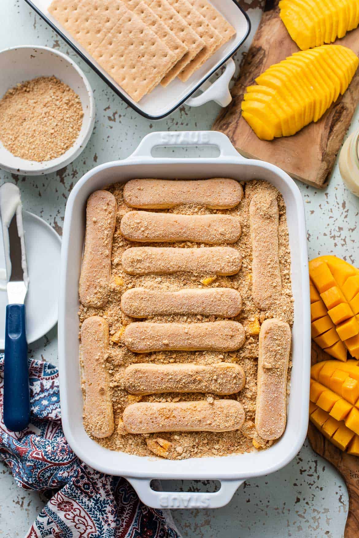 Layering ladyfingers and graham cracker crumbs in baking dish for mango float.