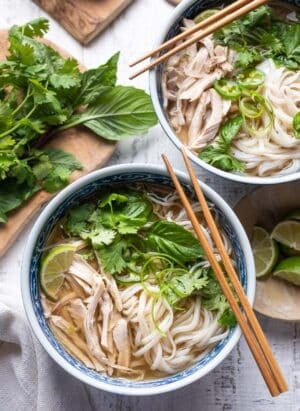 Chicken pho in a bowl with rice noodles, cilantro, basil, and lime.