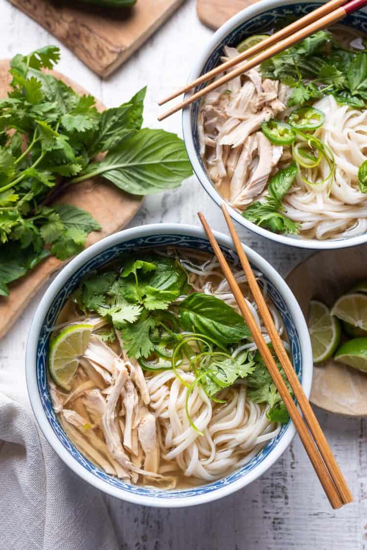 Chicken pho in a bowl with rice noodles, cilantro, basil, and lime.