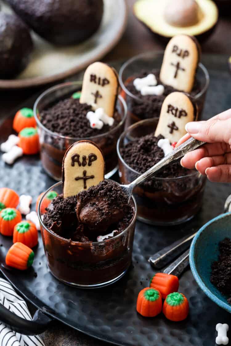 Taking a spoon of Halloween Dirt Cups with Avocado Chocolate Pudding decorated with tombstone cookies.
