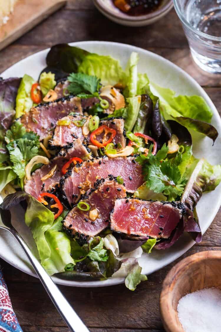 Freshly prepared seared tuna dish surrounded by greens and covered with fresh seasonings.