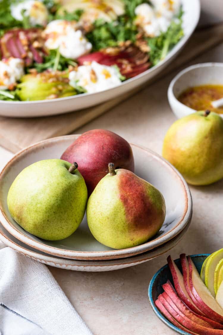 Pears in a bowl with Pear and Burrata Salad in the background.