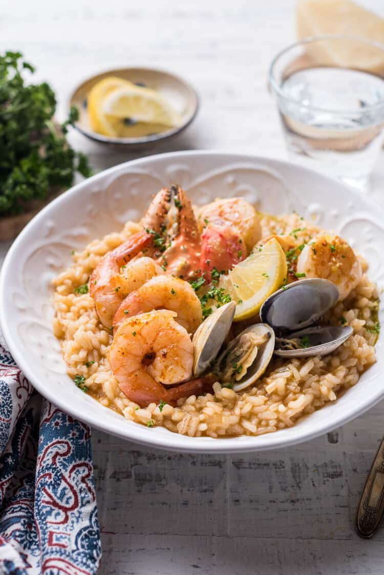 Seafood risotto topped with mixed seafood (shrimp, crab, clams, scallops) in a white bowl.