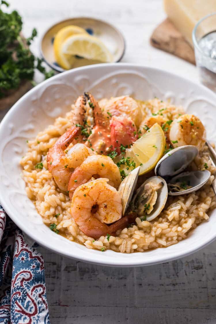 Seafood risotto topped with a variety of seafood (shrimp, crab, clams, scallops) in a white bowl.