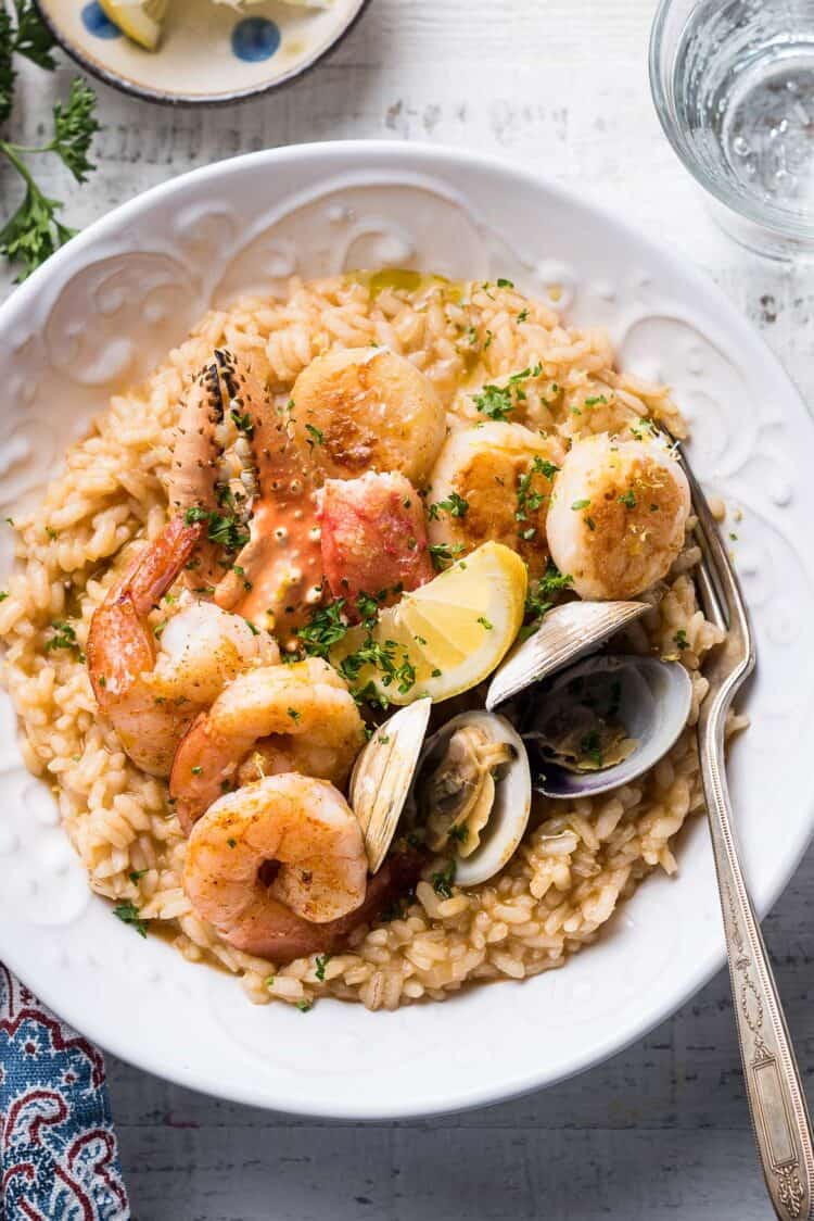 Seafood risotto topped with seafood (shrimp, crab, clams, scallops) in a white bowl.