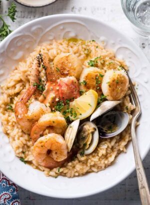 Seafood risotto topped with seafood (shrimp, crab, clams, scallops) in a white bowl.
