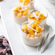 Mango Coconut Tapioca Pudding in individual glass cups on a white serving dish.