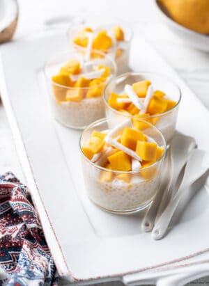 Mango Coconut Tapioca Pudding in individual glass cups on a white serving dish.