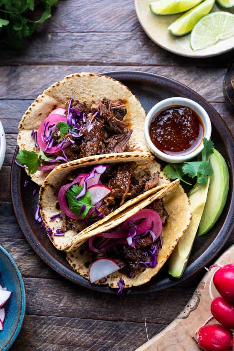 Short rib tacos on a plate with chipotle sauce on the side.